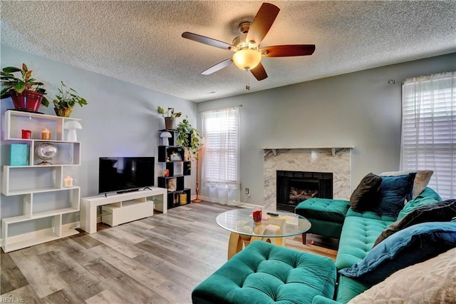 living room with ceiling fan, a textured ceiling, a fireplace, and light hardwood / wood-style floors