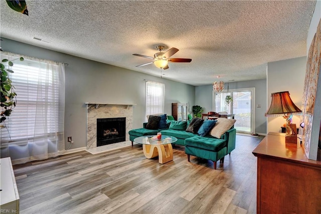 living room with ceiling fan, a high end fireplace, light hardwood / wood-style flooring, and a textured ceiling