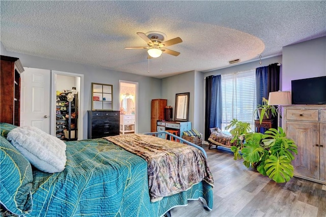 bedroom featuring ensuite bath, light wood-type flooring, a spacious closet, ceiling fan, and a textured ceiling