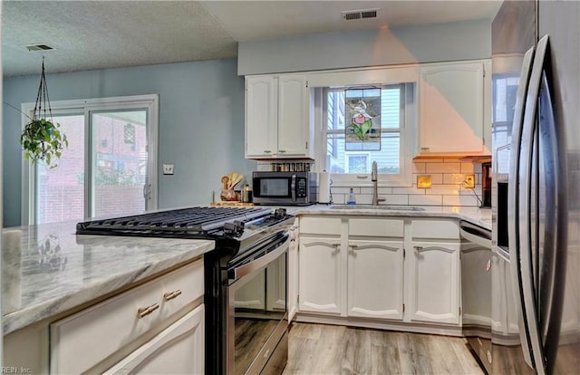 kitchen featuring sink, appliances with stainless steel finishes, light stone countertops, light hardwood / wood-style floors, and white cabinets