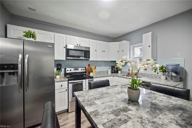 kitchen with light stone counters, white cabinetry, stainless steel appliances, and backsplash