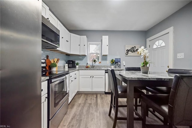 kitchen with sink, stainless steel appliances, light stone counters, light hardwood / wood-style floors, and white cabinets