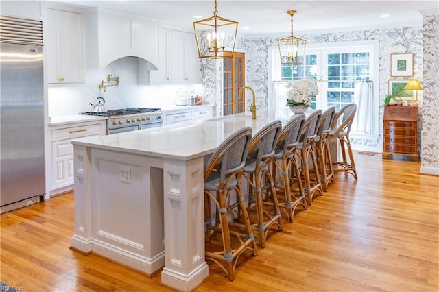 kitchen featuring pendant lighting, sink, white cabinets, premium appliances, and a large island with sink