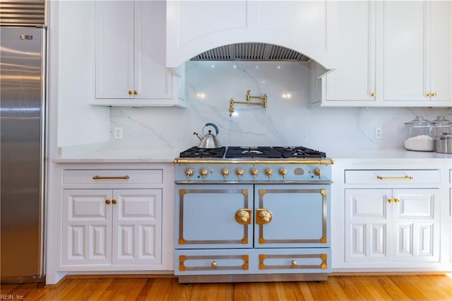 kitchen featuring built in refrigerator, white cabinetry, custom range hood, and range with two ovens