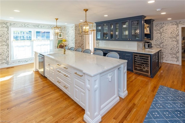 kitchen with sink, light stone counters, dishwasher, beverage cooler, and white cabinets