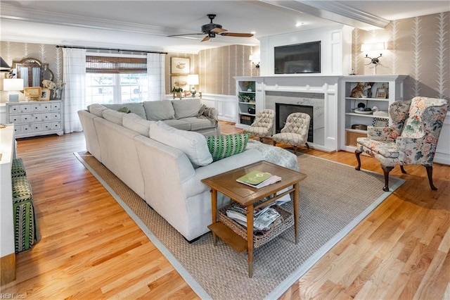 living room featuring crown molding, ceiling fan, a high end fireplace, and light wood-type flooring