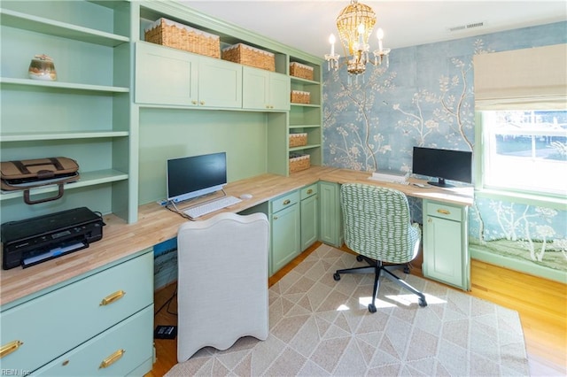 office area with an inviting chandelier, built in desk, and light wood-type flooring