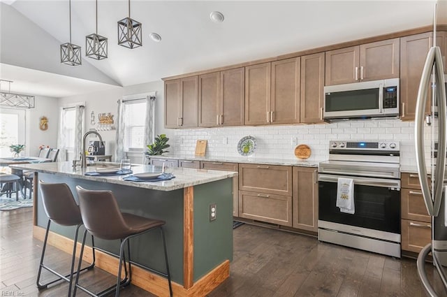 kitchen featuring dark hardwood / wood-style floors, an island with sink, hanging light fixtures, light stone counters, and stainless steel appliances