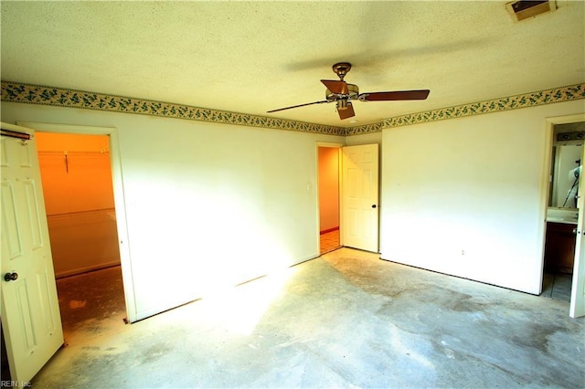 unfurnished bedroom with ceiling fan, a walk in closet, a closet, and a textured ceiling