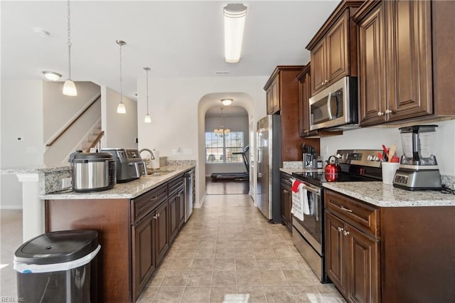 kitchen with a kitchen bar, sink, hanging light fixtures, appliances with stainless steel finishes, and light stone countertops