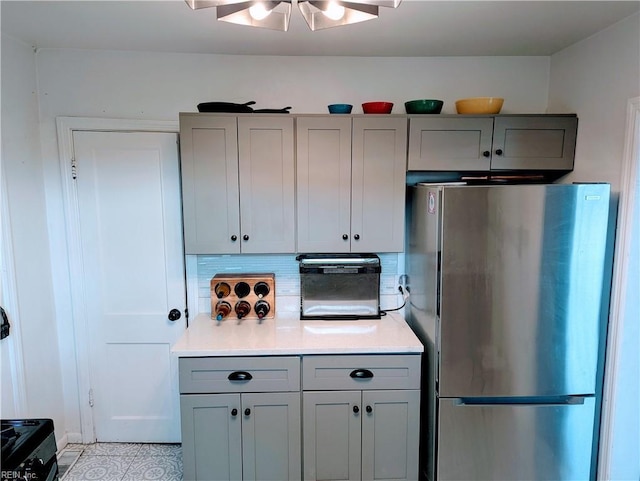 kitchen with gray cabinets, backsplash, and stainless steel refrigerator