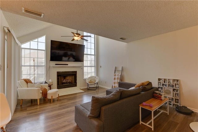 living room with ceiling fan, a fireplace, hardwood / wood-style floors, and a textured ceiling