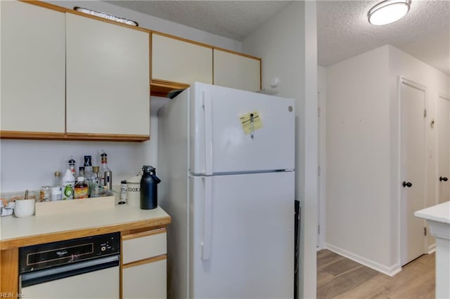 kitchen featuring white fridge, a textured ceiling, white cabinets, and light wood-type flooring