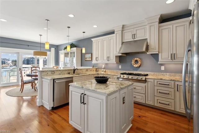 kitchen featuring hardwood / wood-style flooring, hanging light fixtures, stainless steel appliances, a kitchen island, and kitchen peninsula