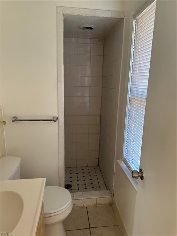 bathroom featuring vanity, toilet, tile patterned flooring, and a tile shower