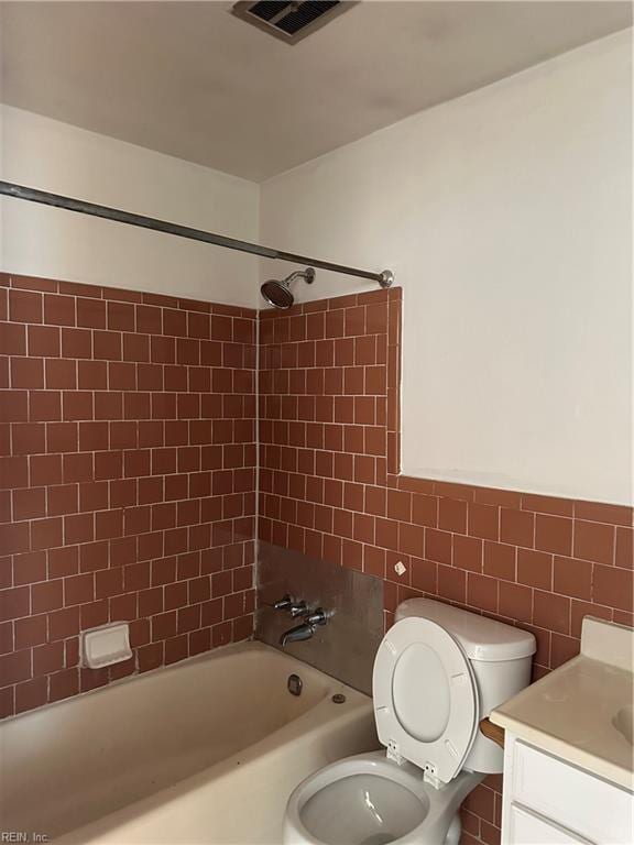 full bathroom with tiled shower / bath, tile walls, vanity, and toilet