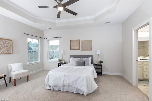 bedroom featuring a raised ceiling, ensuite bathroom, light carpet, and ceiling fan