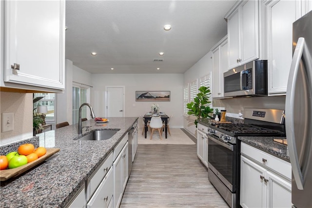 kitchen featuring white cabinetry, stainless steel appliances, sink, and dark stone counters