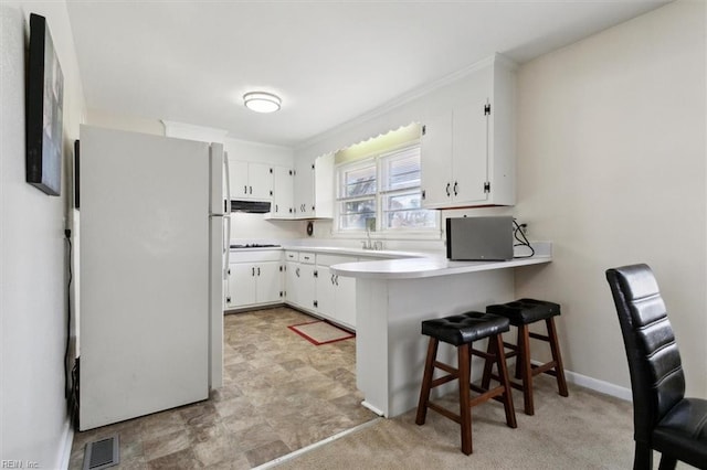 kitchen with white cabinetry, a kitchen breakfast bar, white refrigerator, kitchen peninsula, and crown molding