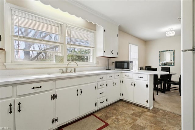 kitchen with white cabinetry, sink, kitchen peninsula, and white fridge