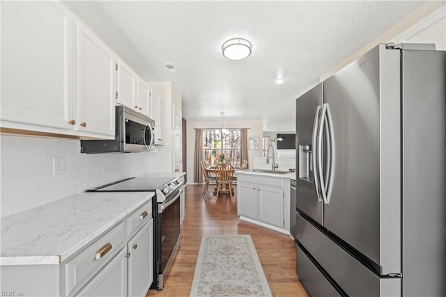 kitchen with sink, hanging light fixtures, appliances with stainless steel finishes, light hardwood / wood-style floors, and white cabinets