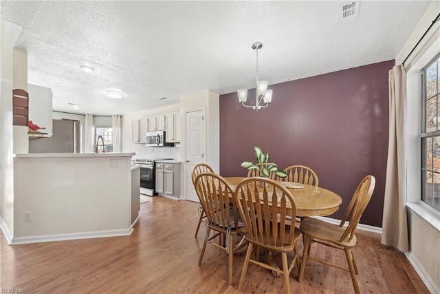 dining space with sink, a textured ceiling, a notable chandelier, and light hardwood / wood-style floors