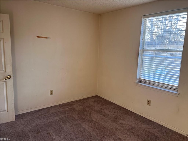 spare room featuring dark carpet, a textured ceiling, and a healthy amount of sunlight