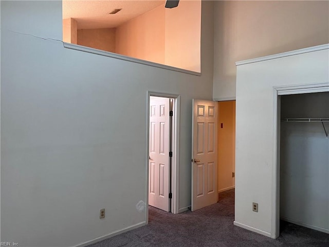 unfurnished bedroom with high vaulted ceiling, a closet, and dark colored carpet