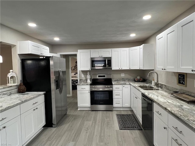 kitchen with sink, white cabinetry, stainless steel appliances, light stone counters, and light wood-type flooring