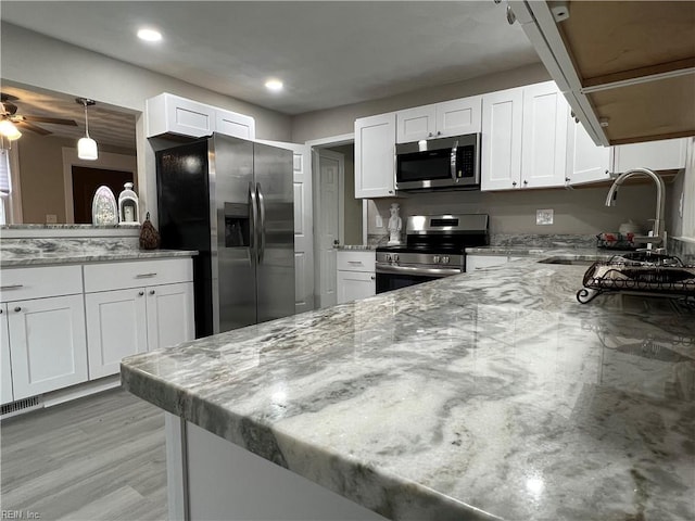 kitchen with sink, white cabinets, light stone counters, kitchen peninsula, and stainless steel appliances