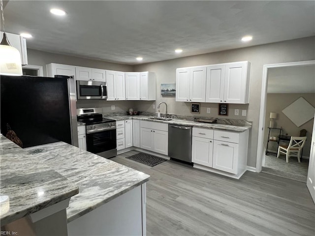 kitchen featuring appliances with stainless steel finishes, sink, white cabinets, hanging light fixtures, and light stone counters