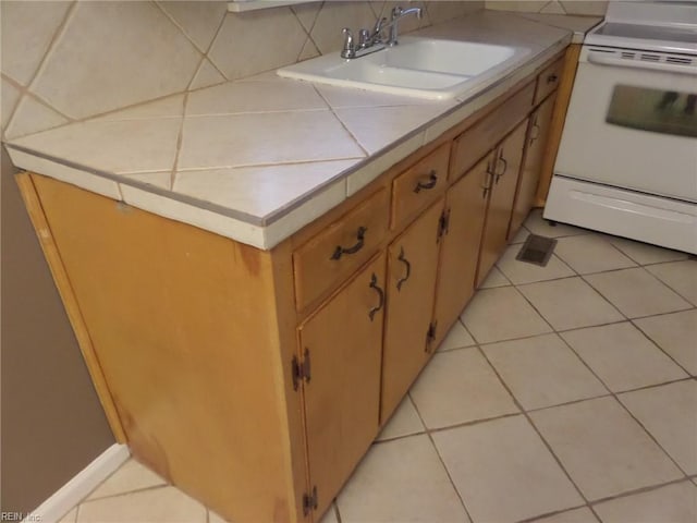 kitchen with electric stove, tile countertops, sink, and light tile patterned floors