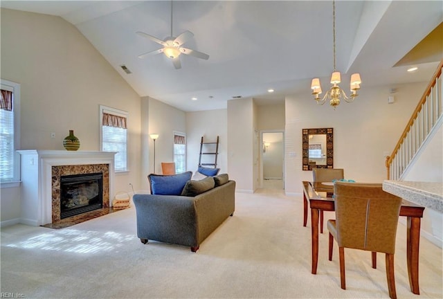 carpeted living room featuring a premium fireplace, ceiling fan with notable chandelier, and high vaulted ceiling