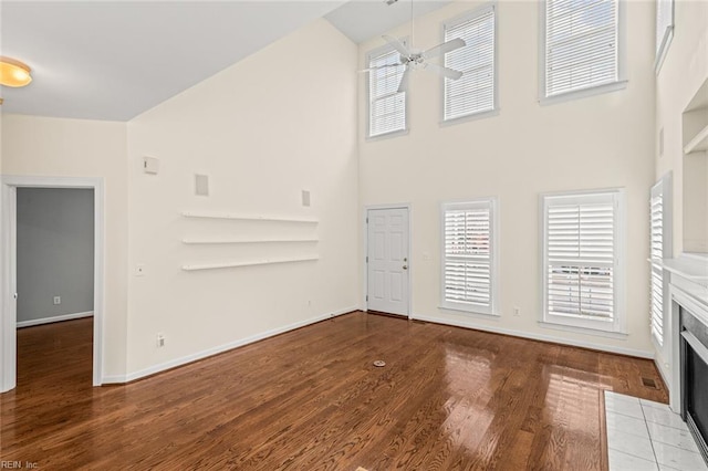 unfurnished living room featuring light hardwood / wood-style flooring, a towering ceiling, a fireplace, and ceiling fan