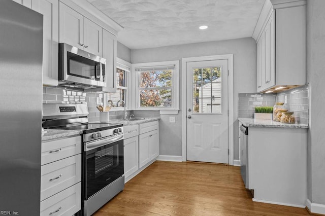 kitchen with stainless steel appliances, sink, white cabinets, and light hardwood / wood-style floors