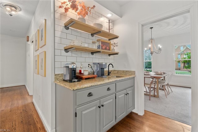 bar with gray cabinets, wood-type flooring, sink, backsplash, and light stone countertops