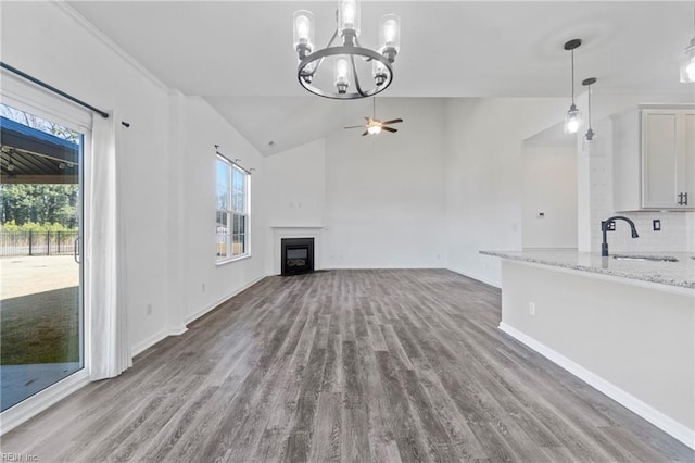 unfurnished living room with hardwood / wood-style flooring, lofted ceiling, ceiling fan with notable chandelier, and sink