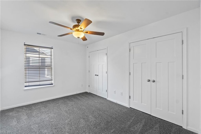 unfurnished bedroom featuring two closets, ceiling fan, and dark colored carpet