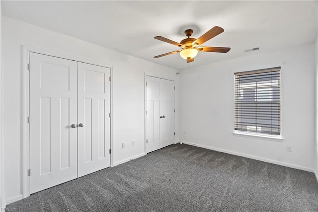 unfurnished bedroom featuring multiple closets, ceiling fan, and dark carpet