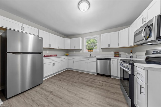 kitchen with light wood-type flooring, appliances with stainless steel finishes, sink, and white cabinets