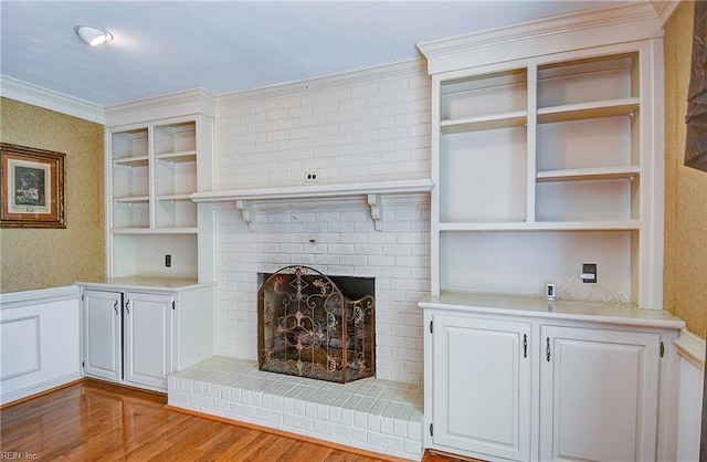 unfurnished living room featuring a brick fireplace, crown molding, built in features, and light wood-type flooring