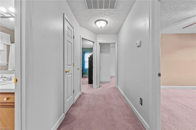 hall with sink, light carpet, and a textured ceiling