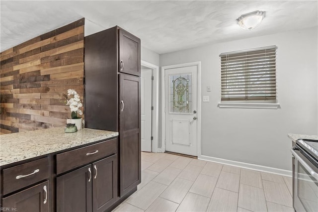 kitchen featuring dark brown cabinetry, electric range, light stone countertops, and wood walls