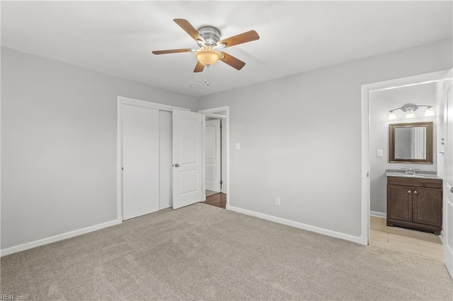 unfurnished bedroom featuring connected bathroom, sink, ceiling fan, light carpet, and a closet