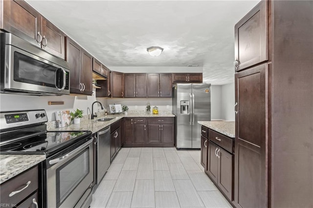 kitchen with sink, dark brown cabinets, light stone countertops, and appliances with stainless steel finishes