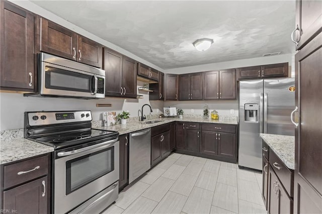 kitchen with appliances with stainless steel finishes, light stone countertops, sink, and dark brown cabinets