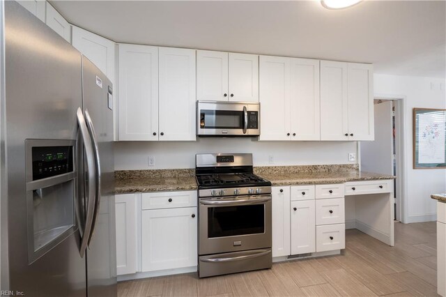 kitchen with stainless steel appliances, white cabinetry, dark stone countertops, and light hardwood / wood-style floors