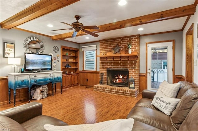 living room with built in features, beamed ceiling, light hardwood / wood-style floors, crown molding, and a brick fireplace