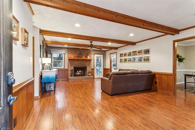 living room featuring beamed ceiling, wood walls, a fireplace, and light wood-type flooring