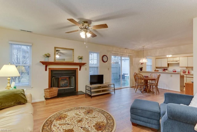 living room with ceiling fan, a textured ceiling, and light hardwood / wood-style floors